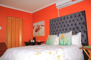 Un dormitorio con una cama grande con una pared naranja. en 7th Dimension Guesthouse, en Zeerust