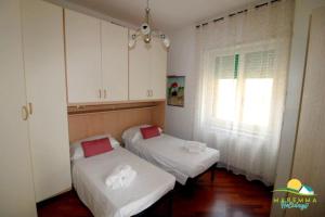 フォッローニカにあるMaremma Holidays : Fiore Apartmentの白いキャビネットと窓が備わる客室で、ベッド2台が備わります。