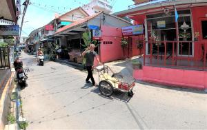 um homem empurrando um carrinho para baixo de uma rua em Taphouse em Hua Hin