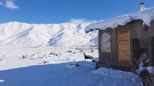 una casa cubierta de nieve con una silla en la nieve en CABAÑA MELIPAL LOS MOLLES en Malargüe