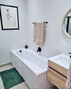 Baño blanco con bañera y lavamanos en Palm On Rock - 1 bedroom,kitchenette & full bathroom. en Bloemfontein