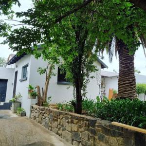 a white house with trees and a stone wall at Palm On Rock - 1 bedroom,kitchenette & full bathroom. in Bloemfontein