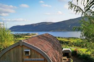a wooden building with a brick roof next to a lake at The Highland Bothies Glamping in Ullapool