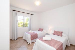 2 camas en una habitación blanca con ventana en Villas Geisan, en Ciutadella