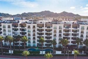 um grande edifício branco com palmeiras e montanhas em Condo Maravilla - New luxurious condo 300mt from the beach em Cabo San Lucas