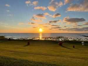 una puesta de sol sobre el océano con un campo de hierba en Nordseetraum - Ferienhaus Wolke, en Friedrichskoog