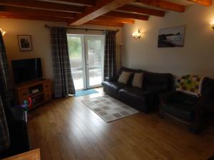 a living room with a leather couch and a television at Burry Farm Cottage in Swansea