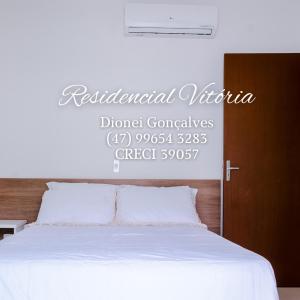 Un dormitorio con una cama blanca con un letrero encima. en Residencial Vitória, en Bombinhas