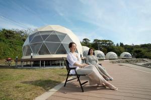 dwie kobiety siedzące na krześle przed kopułą budynku w obiekcie TADAYOI 海士グランピング 