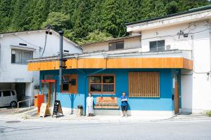 2 personnes debout devant un bâtiment bleu dans l'établissement Guest House POST INN, à Tenkawa