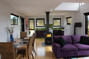 ein Wohnzimmer mit einem lila Sofa, einem Tisch und einem Herd in der Unterkunft Far South Eco-Cabin, Southern Tasmania in Lune River