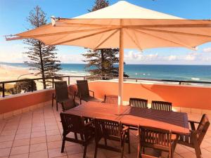 a wooden table with chairs and an umbrella on the beach at The Beach Retreat Coolum in Coolum Beach