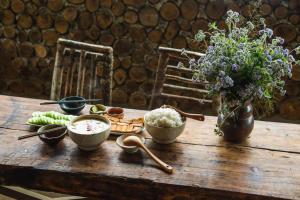 a wooden table with bowls of food and a vase of flowers at 1941M Homestay Tà Xùa in Bắc Yên