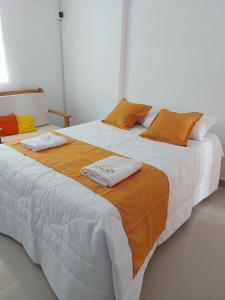 Cama grande con sábanas y almohadas de color naranja y blanco en Majestic Mical en Yurimaguas