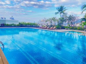 a large blue swimming pool with chairs and palm trees at Laemtong Serviced Apartment in Si Racha