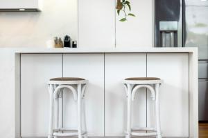 una cocina con armarios blancos y 2 taburetes blancos en Holiday home Alex Headland, en Alexandra Headland
