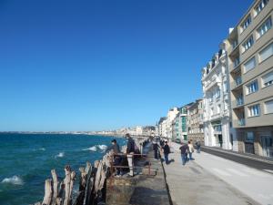 a group of people walking on a sidewalk next to the ocean at SAINT MALO bel appartement plain pied 300 m gare prés plage du sillon Intramuros a pied in Saint Malo