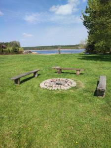 two benches and a fire pit in a field with a lake at Gościniec IBIS in Czarna Wieś