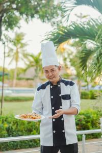 Un ragazzo con un cappello da chef che tiene un piatto di cibo di Tanga Beach Resort & Spa a Tanga