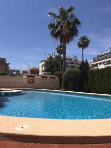 a large blue swimming pool with palm trees and buildings at Lovely one bedroom unit with balcony and pool in Denia
