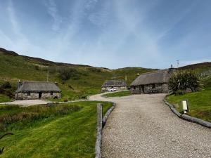 a gravel road leading to two buildings with thatched roofs at Tigh Phadraig at Marys Thatched Cottages in Elgol