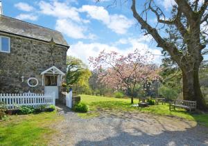 una vieja casa de piedra con una valla blanca y un árbol en The Stables en Whitland
