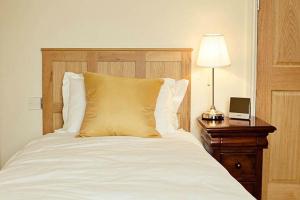 a white bed with a wooden headboard and a table with a lamp at Kings Arms Hotel in Bicester