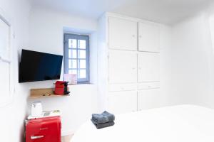 une chambre blanche avec une télévision et une valise rouge dans l'établissement Villa Sibille - Plein centre de Saint-Tropez, à Saint-Tropez