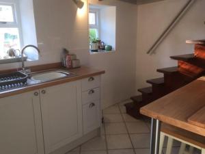 uma cozinha com armários brancos, um lavatório e escadas em Historic school room em Helston