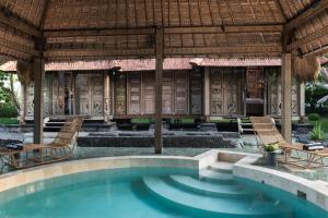 a pool in front of a resort with chairs and a pavilion at Beachfront Villa Pryaniki Tabanan in Tabanan