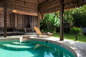 a resort pool with a chair and a house at Beachfront Villa Pryaniki Tabanan in Tabanan