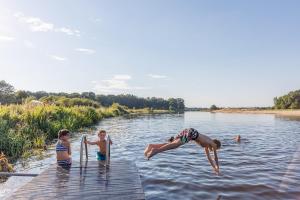 trójka dzieci skaczących z przystani do rzeki w obiekcie Huttopia de Roos w mieście Stegeren