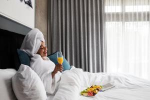 a woman laying in bed with a glass of orange juice at The Capital Melrose in Johannesburg