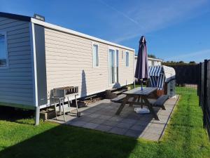 a picnic table and an umbrella on a patio next to a caravan at Campingland Ostsee - Mobilheim 155Meerluft in Schashagen