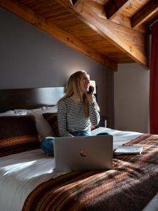 a woman talking on a phone while sitting on a bed with a laptop at Hotel Crans Montana in San Carlos de Bariloche