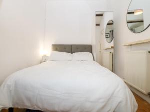 1 cama blanca en un dormitorio blanco con espejo en Bwthyn Taid a Nain, en Bodorgan