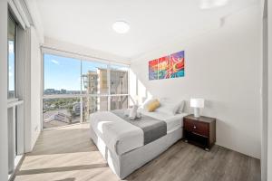 a white bedroom with a bed and a large window at Oxygen Apartments in Brisbane