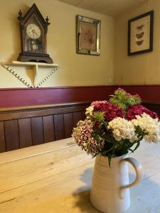 a vase filled with flowers on a table with a clock at Kings Head Low House in Laxfield