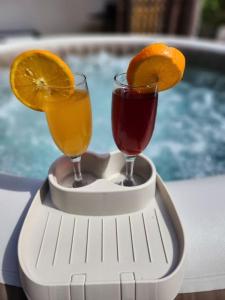 two glasses of juice and oranges on a holder next to a pool at Villa Marilou - Les pieds dans l'eau in Quartier du Fond Fleuri
