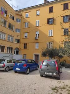 trzy samochody zaparkowane na parkingu przed żółtym budynkiem w obiekcie Karmen w mieście Zadar