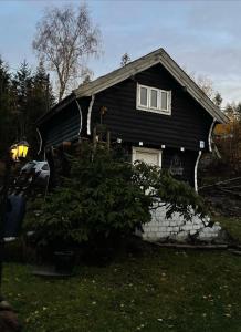 een zwart huis met een boom ervoor bij Stabbur Steinbekken, back to basic primitive overnight in Eidsvoll