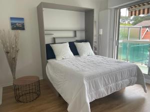 a bedroom with a white bed with a large window at Appt calme au centre du Moulleau in Arcachon