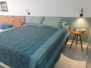 a bedroom with a bed with a blue comforter and a table at Bahia Flat - Flats na Barra in Salvador