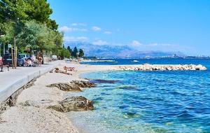 a beach with people sitting on the rocks and the water at BayStay in Kaštela