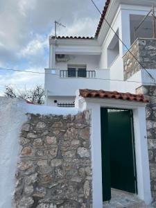 a white house with a green door and a stone wall at Tasos_Studios&Apartments in Kranidi