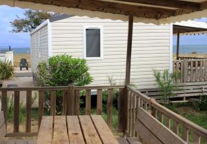 a white house with a porch and a wooden deck at Mobil home vue mer camping Tohapi in Vias