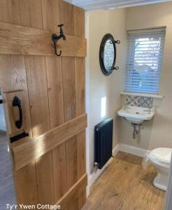 a bathroom with a wooden door with a toilet and a sink at Tyr Ywen Cottage in Abergavenny