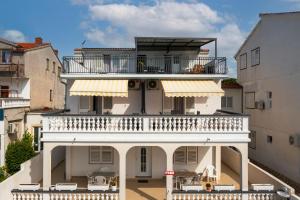 een groot wit huis met een balkon en stoelen bij Apartment and Rooms Dalmatiko in Vodice