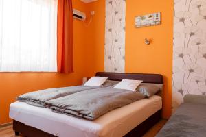 Cama en habitación con paredes de color naranja y ventana en Piknik Vendégház, en Bogács