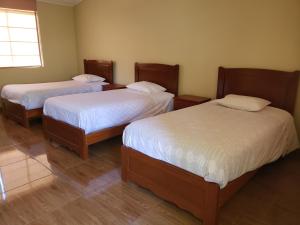 Habitación con 3 camas, sábanas blancas y ventana. en Condominio La Curva en Churín
